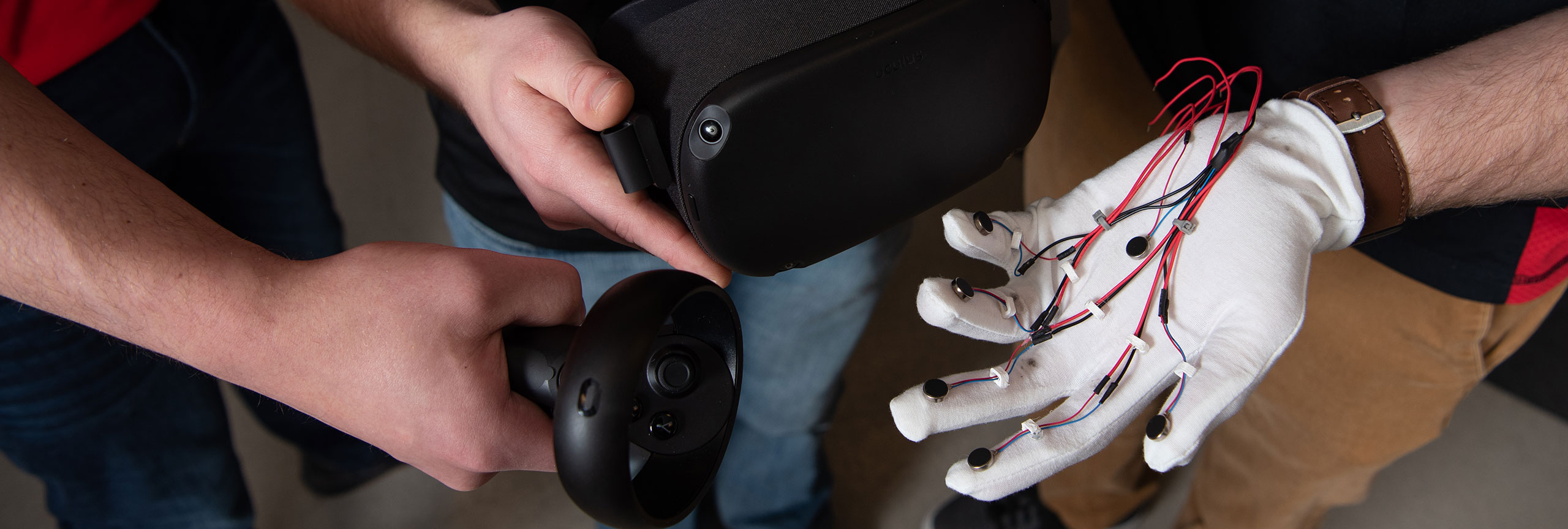 Hands interacting with a VR controller and headset, alongside a glove with wires and sensors.